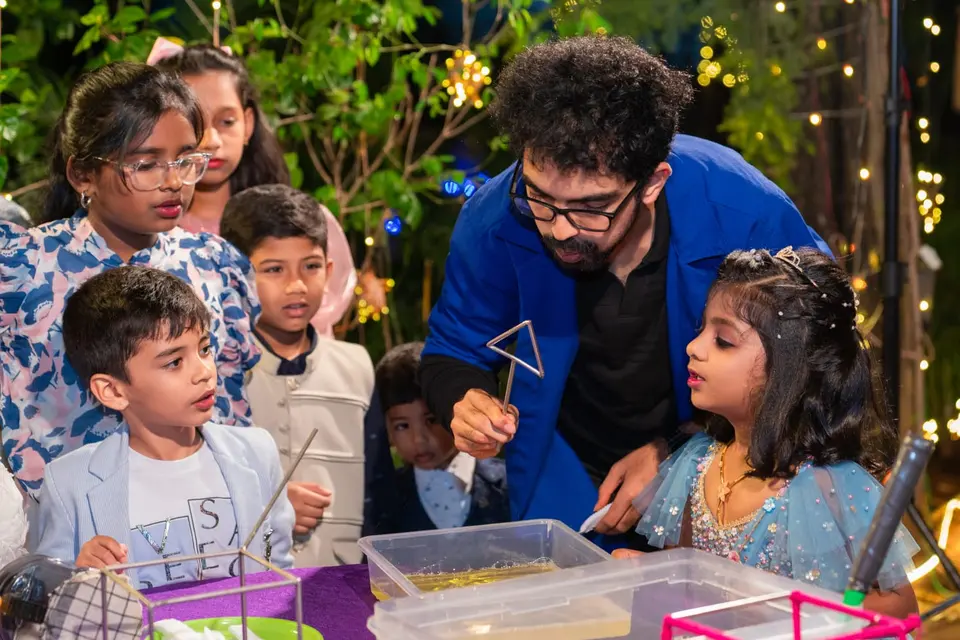 A MakerMasti host leaning over a tray of bubble solution while a crowd of children watch