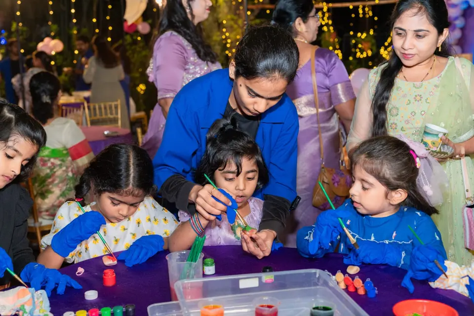 Children in gloves at a craft table of paint pots and thread spools, working with two MakerMasti hosts