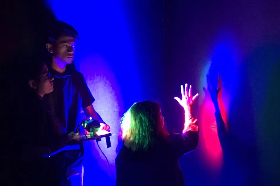 A child silhouetted with glowing hands raised in a darkened room lit by UV light