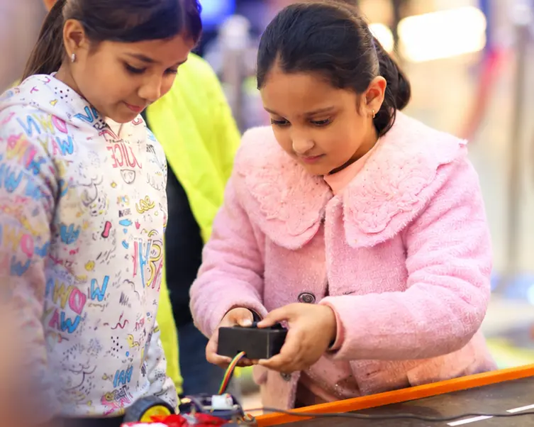 Two girls steering a robot car they built along a track at a MakerMasti science festival