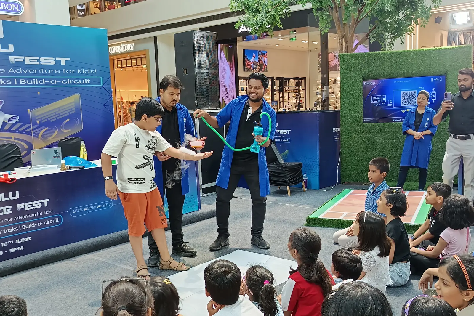 A MakerMasti presenter on stage running a demonstration for a seated crowd of children