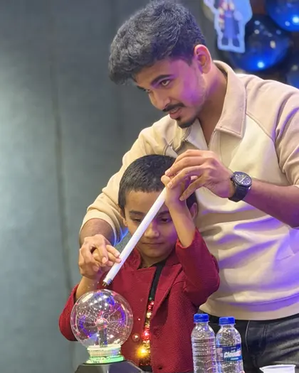A boy touching a plasma globe with a rod, the filaments bending toward his hand