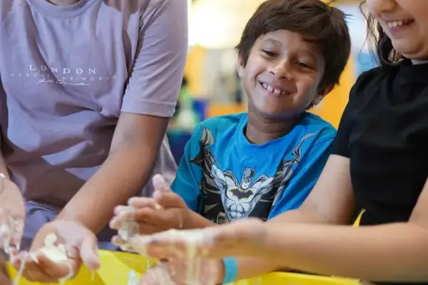 Two children laughing with their hands buried in a tray of bright yellow slime