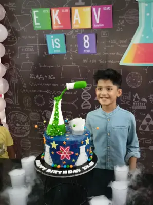 birthday child with science themed cake placed on a table