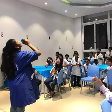 science host demonstrating a fund science activity to kids wearing blue lab apron