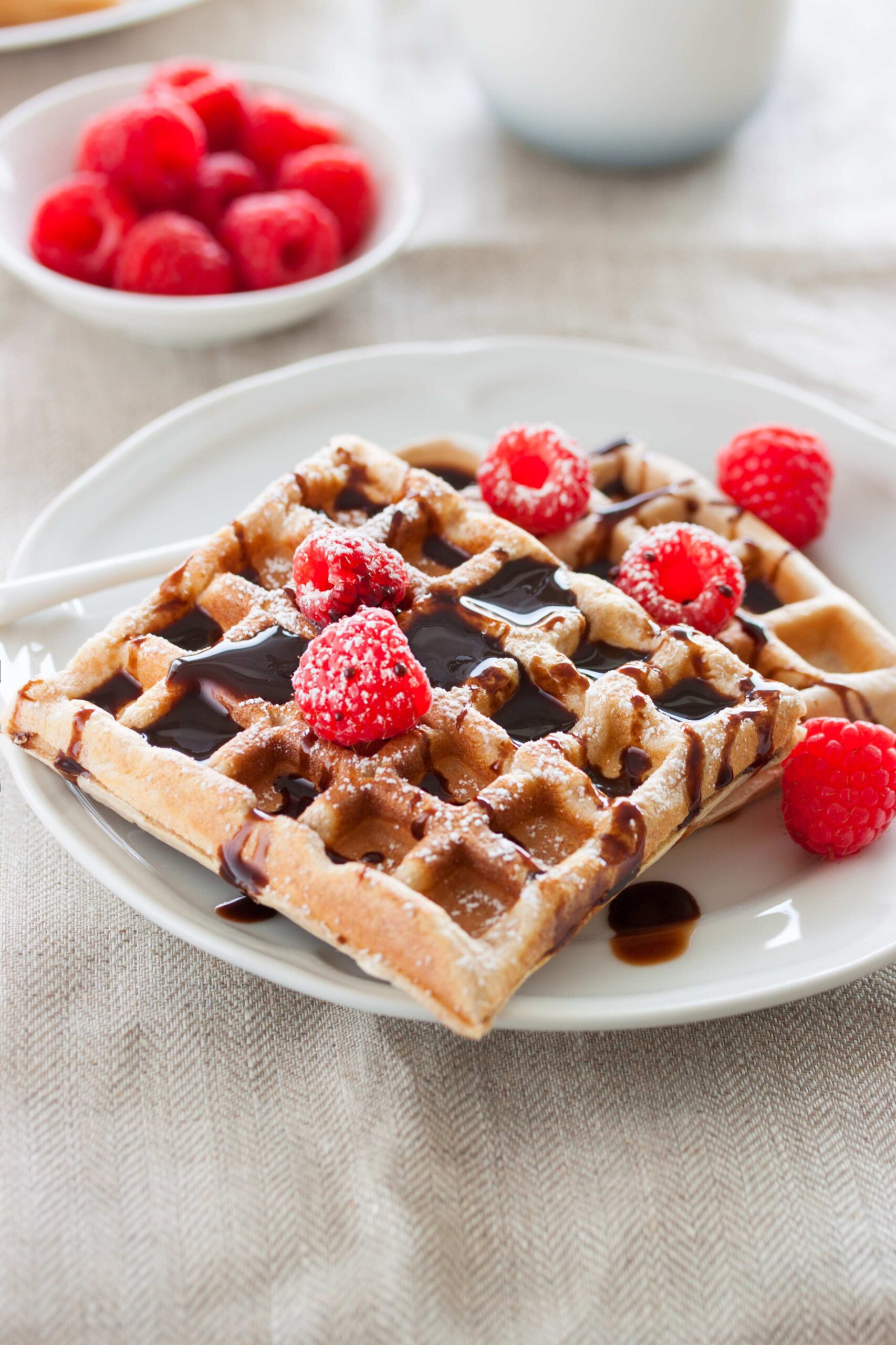 Tasty homemade waffles with raspberries and chocolate sauce ready for breakfast, closeup, selective focus